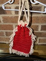 Front view of red crocheted purse with cream fringe and strap