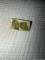 Front view showing twin green leaf design on glazed ceramic surface