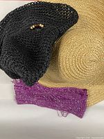 Group view of black crochet hat, tan straw hat, purple sparkle scarf