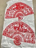 Two identical red paper-cut fan hangings on plastic backing