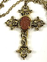 front view of ornate cross pendant with orange stone and portion of chain