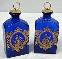 Front view showing both cobalt blue glass bottles with gold floral decoration