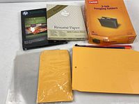 Lot overview displaying HP brochure paper box, Southworth résumé paper box, Staples hanging folders box, manila envelopes pack, clear poly sleeves