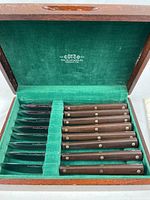 Open wood box showing eight wood-handled Cutco steak knives set in green felt