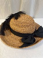Front view of tan straw hat showing ribbon band, bow, feather