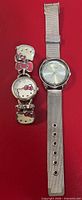 Hello Kitty bracelet watch and Ellen Tracy silver-tone watch side by side on red background