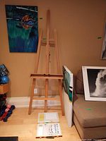 Easel standing against wall with paint set open on floor and canvases behind