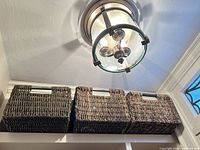 Three woven rectangular baskets on shelf under ceiling light