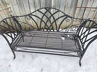 Full view of black metal bench in snow, showing overall design