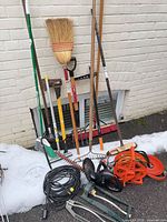 Group of long-handled tools, hedge trimmers, cords and hose gear against wall