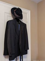 Dark pin-stripe double-breasted suit jacket on hanger with tie and fedora