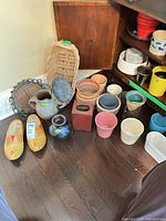 group of items on floor: clogs, multiple pots, vases, baskets, metal trivet