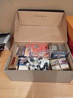 Cardboard box with assorted trading cards, Pokemon package, Donruss box, plastic bag of round pieces, and sleeves