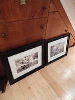 Two framed prints leaning against wood cabinet