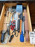 Open drawer showing rolling pin, spatulas, scissors, grater, pasta server, small spoons, whisk, bottle stopper and more