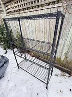 Full view of black metal wire shelving unit with four shelves on snow background