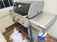 Front angled view of Weber Genesis II grill showing three control knobs, side shelves, propane tank shelf