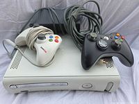 Front angled view of Xbox 360 console with controllers and power brick visible