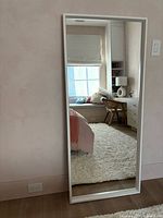 Front view of full-length white wood frame mirror leaning against wall