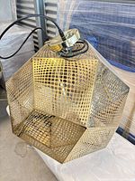 Full view of perforated brass geometric pendant light with cord and canopy