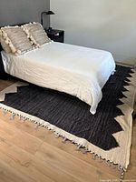 Full view of rug under bed showing black field, beige zig-zag border, fringe
