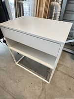 Front view of white nightstand showing drawer, open shelf, and metal frame