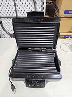 Grill opened showing both ribbed plates and power cord
