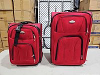 Front view of large and small red Ricardo softside suitcases showing zip compartments and pull handles
