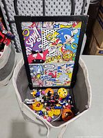 Framed Sonic print standing in bin with assorted figures and watch visible