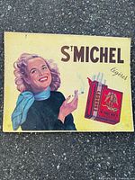 Front view of St Michel cardboard sign with woman and cigarette pack illustration