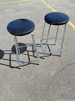 Two chrome bar stools with black vinyl seats shown outdoors