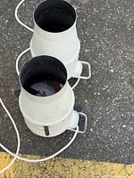 Top view of two white cylindrical steel spotlights showing openings and cords