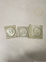 Three 1964 Kennedy half dollars in protective sleeves