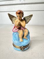 Front view of porcelain angel trinket box showing cherub, blue base, hinged clasp