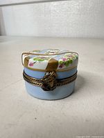 Front view of round hand-painted Limoges porcelain trinket box showing clasp and floral design