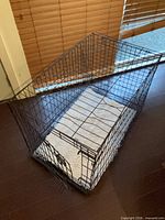 Overall view of black metal wire crate with white fleece pad inside