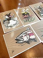 Four kraft paper prints: loon, thistle with bee, salmon, partial alpine floral scene