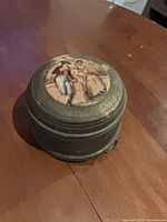 Top view of gray metal music box with Victorian couple lithograph on lid