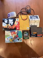 Lot overview showing SNES mouse, N64 boxes, GoldenEye manual, Tron manual, Intellivision cartridges and Pitfall! cartridge
