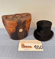 Leather oval carrying case beside black top hat