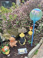 Group shot of gazing globe, four animal figures and yard sign in garden bed