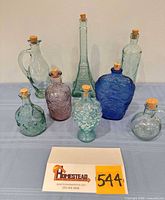 Front view of all eight coloured glass bottles with corks