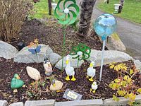 Overall view of duck figurines, metal flowers and glass globe in garden bed
