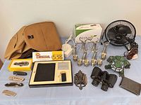 Overview of entire lot on tabletop showing bag, tools, electronics, fan, lamp, shot glasses, bird feeder