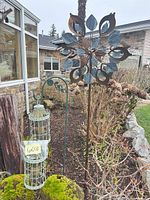 Bird feeder on mossy stump beside tall floral wind spinner