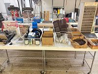 Overview of table with cabinet, baskets of hardware, grates, sprinkler heads, light fixtures