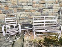 Full view of rocker, side table and glider bench arranged against stone wall