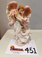 Front left view of angel figurine showing pose, grapes, wings, gown