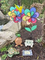 All six garden decor items arranged by pond: pottery turtle, metal turtle, porcelain frog, yellow glass bird on stake, two pinwheel flowers