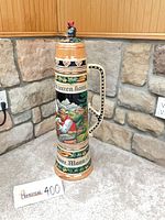 Full view of tall West Germany ceramic beer stein showing handle side and lid with figure